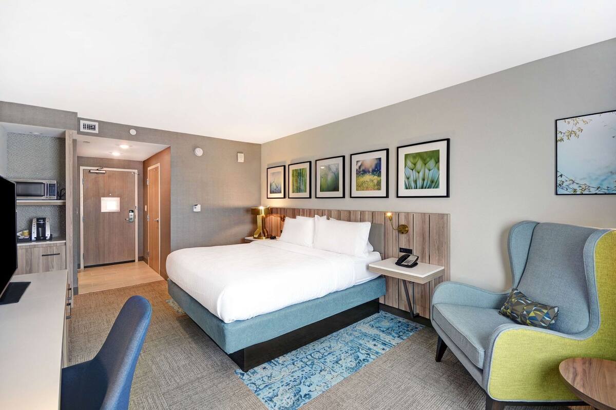 A hotel room with a bed, bedside table, chair, desk, and microwave.