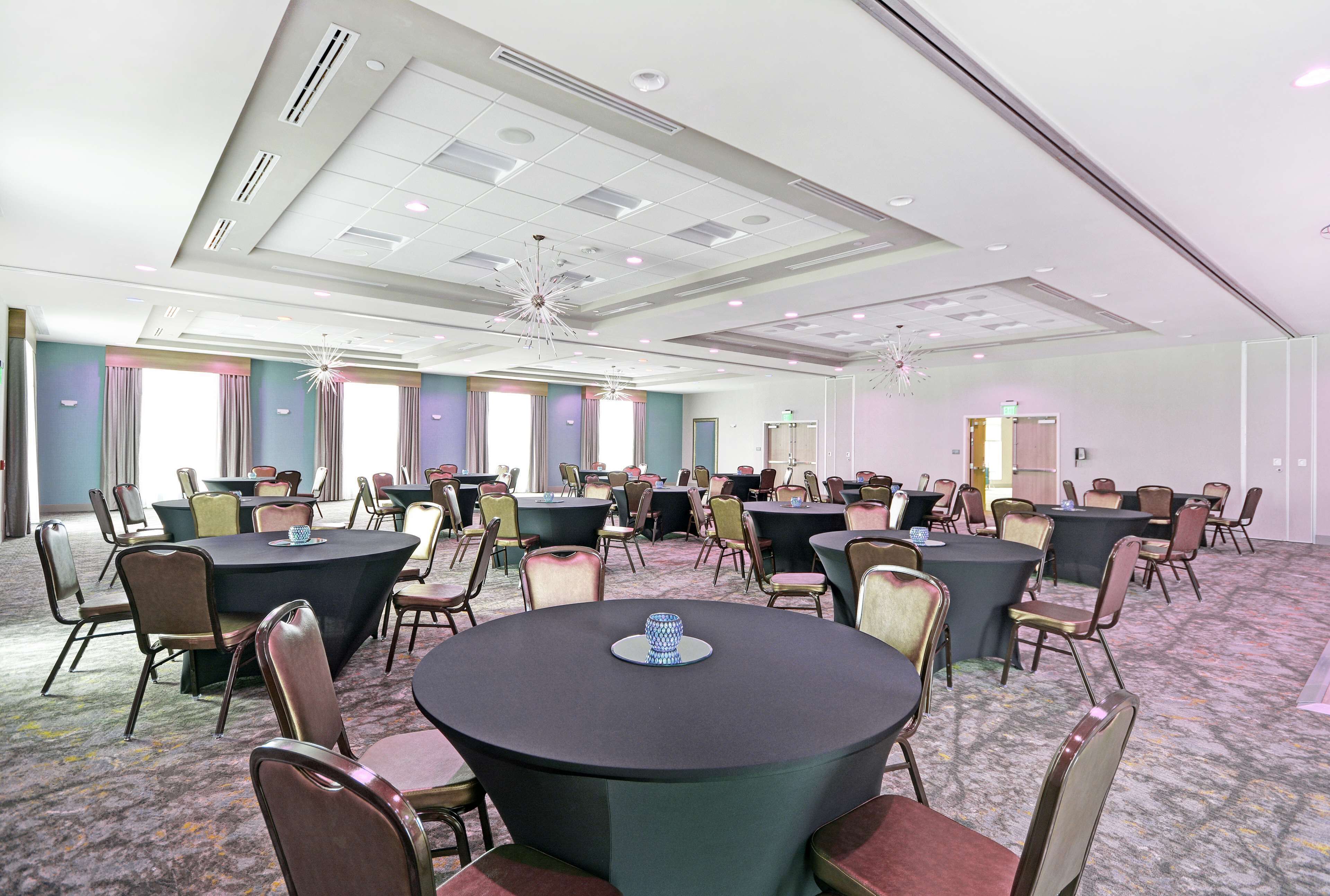 A conference room with multiple tables and chairs, ceiling lights, and a carpeted floor.