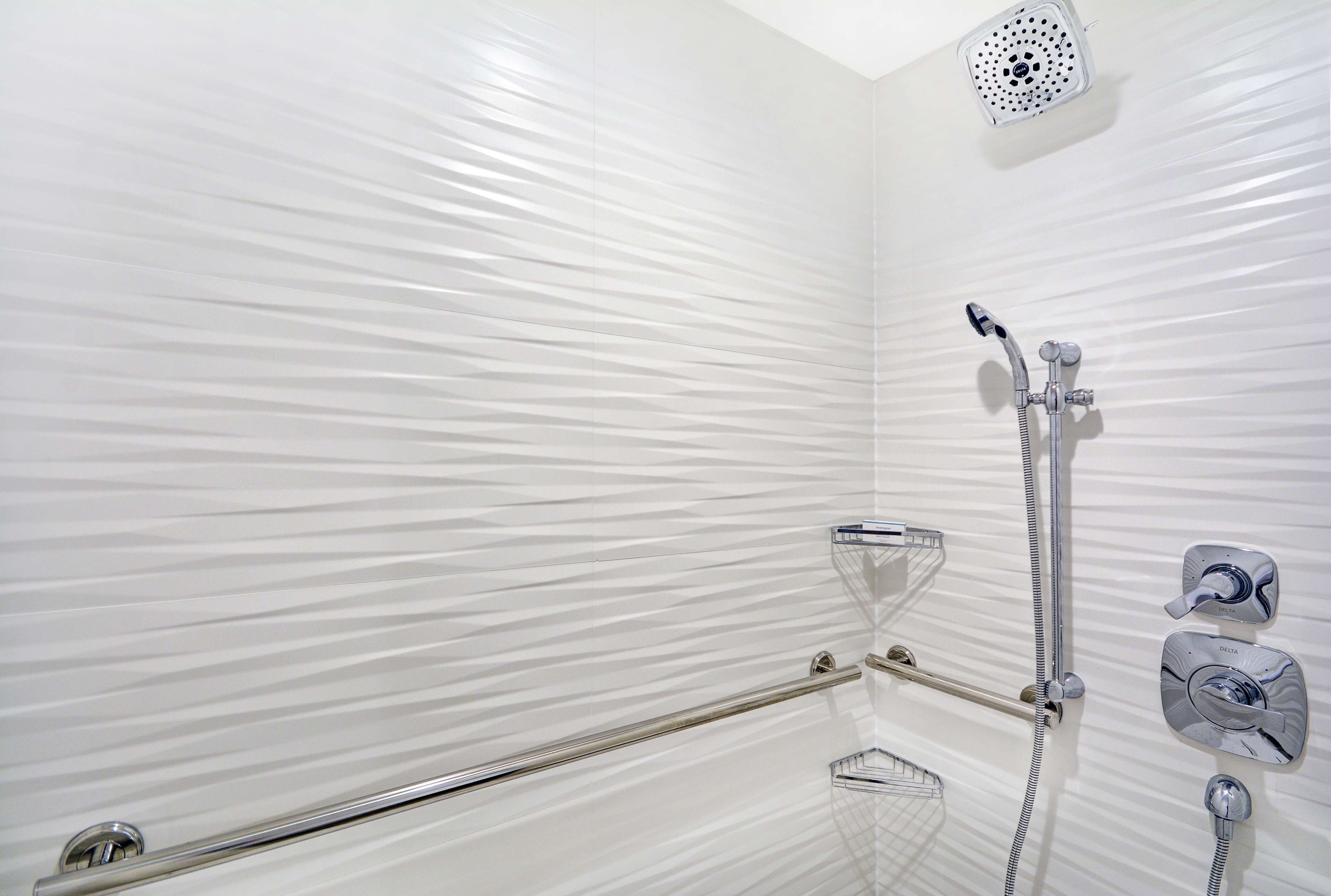 A modern bathroom with a shower, grab bars, and a handheld showerhead.
