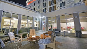 Un hôtel Hilton Garden Inn doté d’un espace extérieur aménagé, d’un foyer et de grandes fenêtres donnant sur l’intérieur.