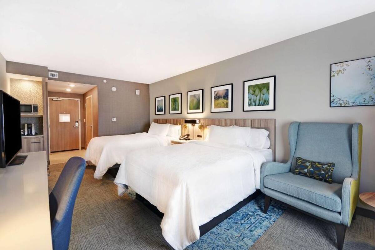 A hotel room with two beds, a desk, a chair, and a television.