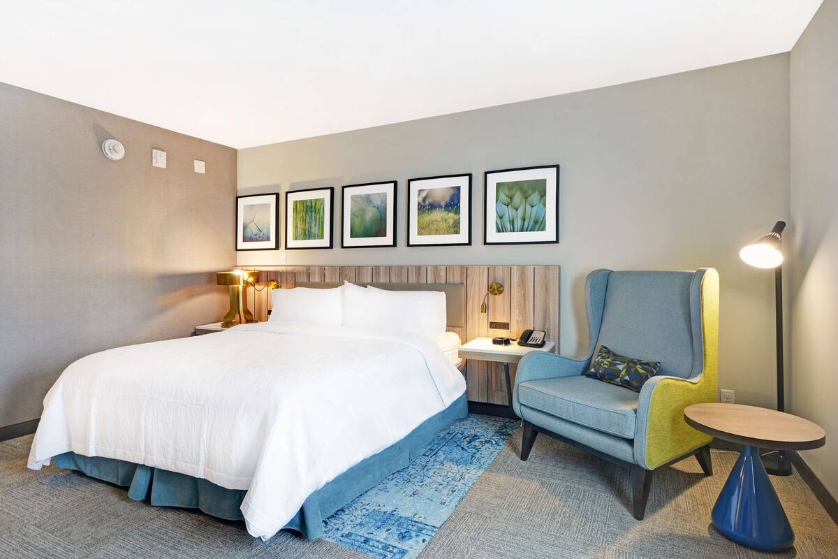 A hotel room with a large bed, a desk, a chair, and framed pictures on the wall.