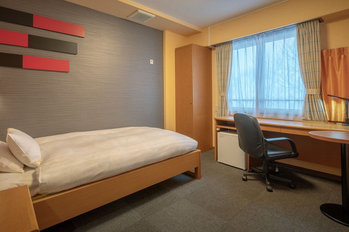 A hotel room with a bed, desk, chair, and a window with curtains.