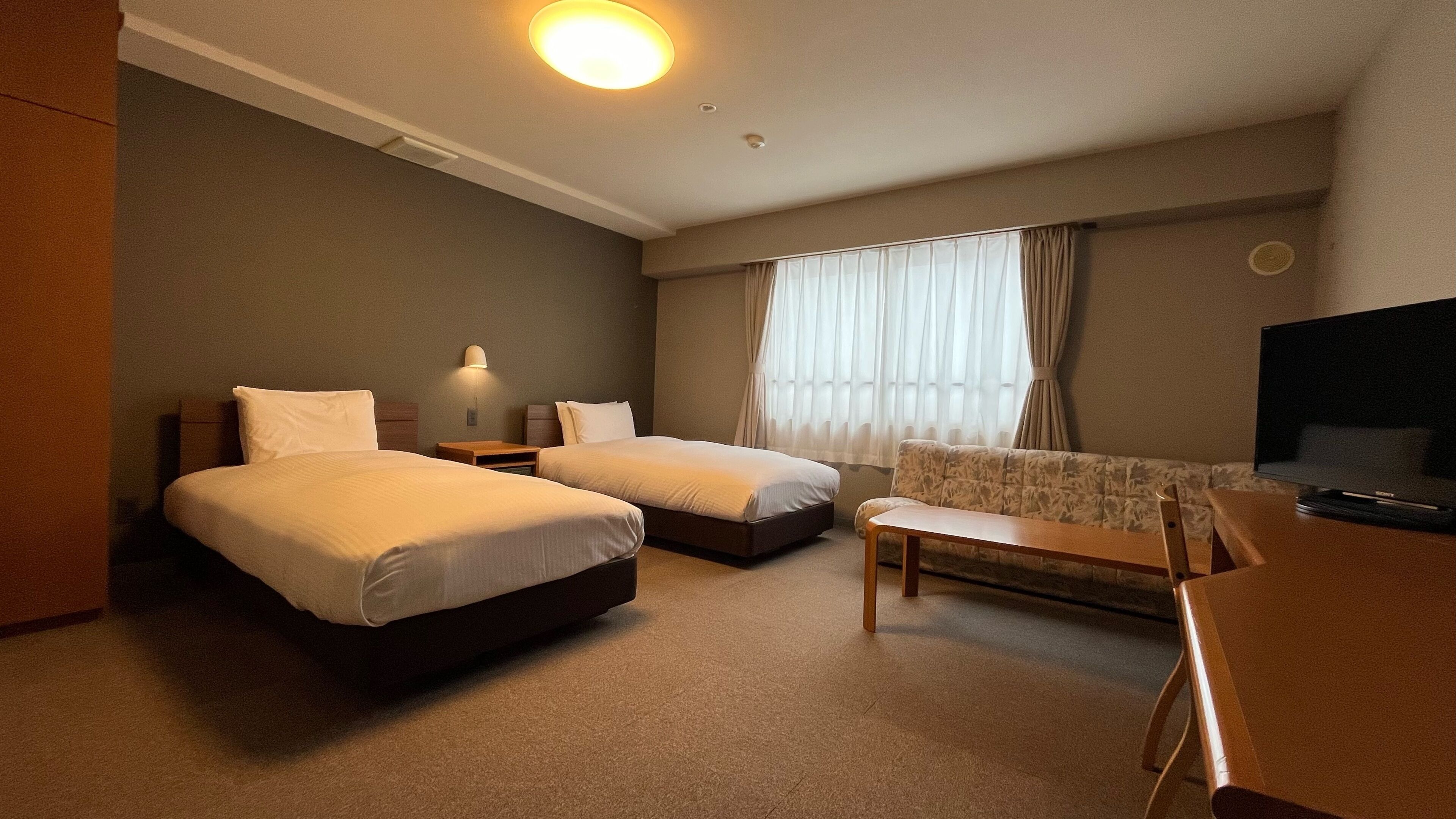 A hotel room with two beds, a sofa, a TV, and a window with curtains.