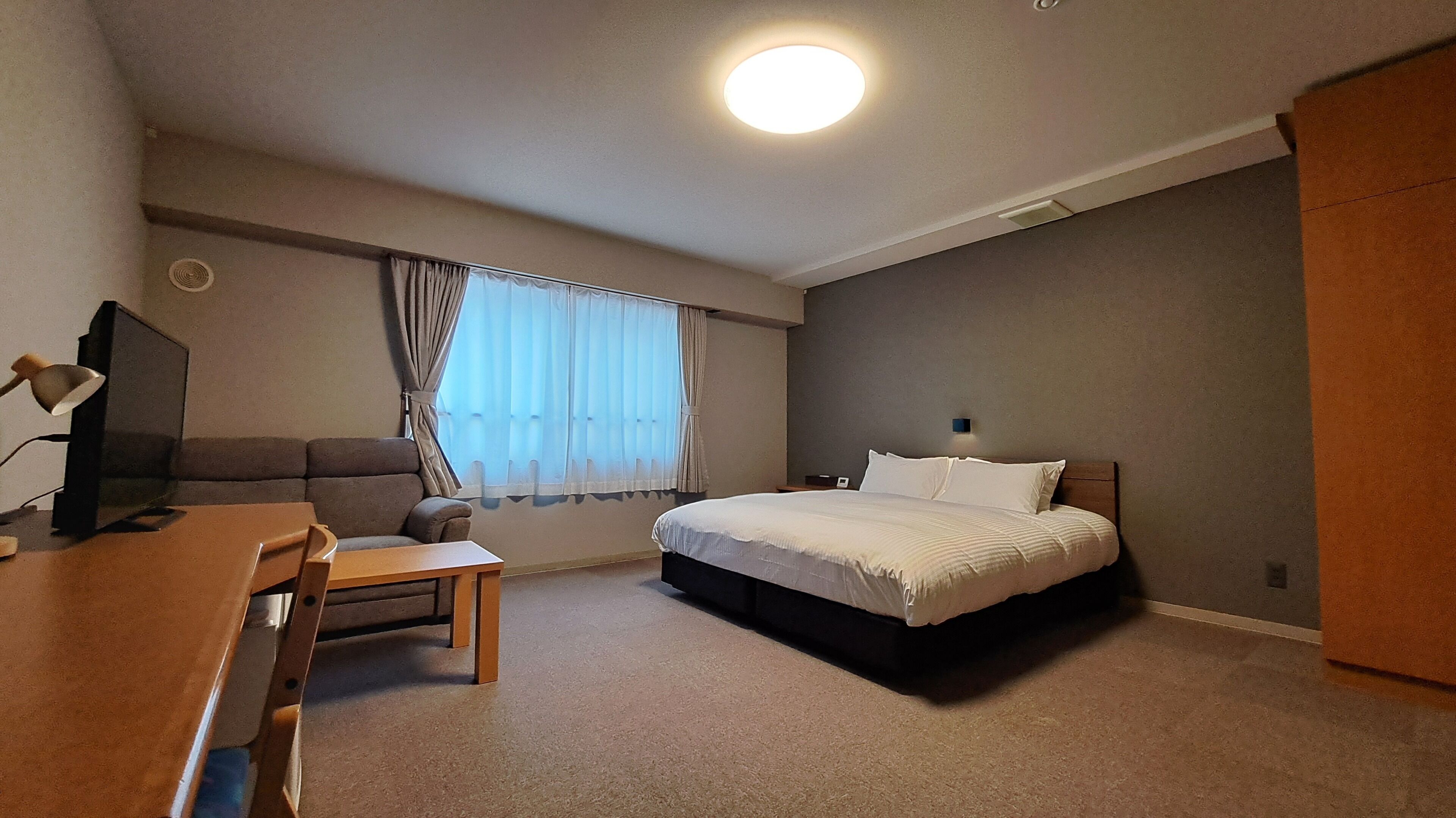 A hotel room with a bed, a desk, a chair, a television, and a window with curtains.