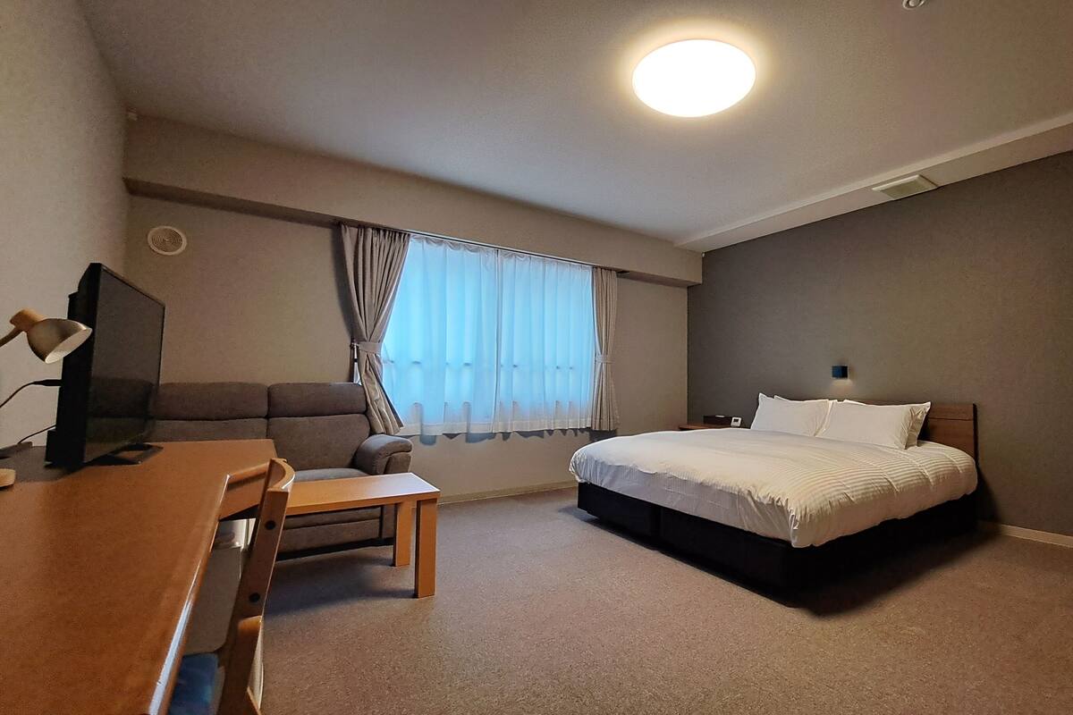 Hotellihuone, jossa on sänky, työpöytä, tuoli, televisio ja ikkuna, jossa on verhot.