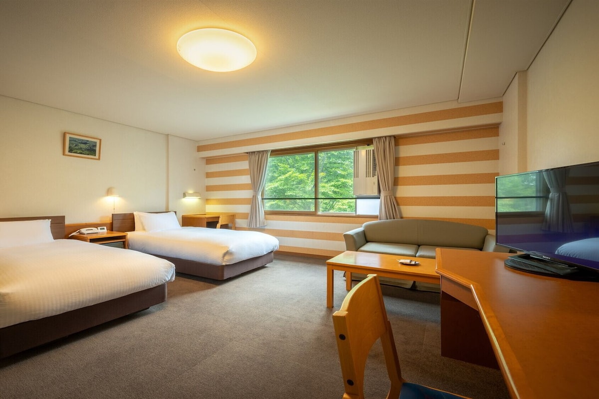 Hotellihuone, jossa on kaksi sänkyä, työpöytä, tuoli, televisio ja ikkuna, jossa on verhot.