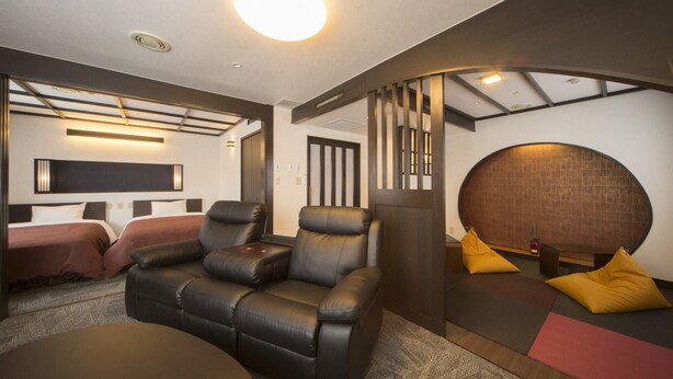 A modern hotel room with a sofa, a bed, a massage table, and a wall-mounted TV. - Yamadake Onsen Resort Shin Tamagawa Onsen (Senboku)