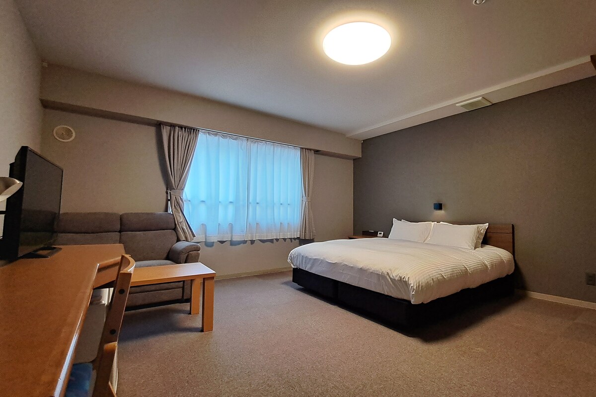 Een hotelkamer met een bed, een bureau, een stoel, een televisie en een raam met gordijnen.