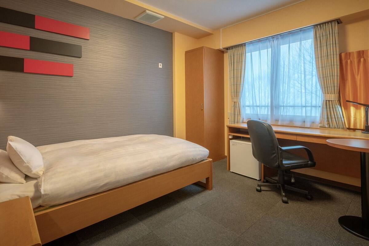 Hotellihuone, jossa on sänky, työpöytä, tuoli ja ikkuna, jossa on verhot.