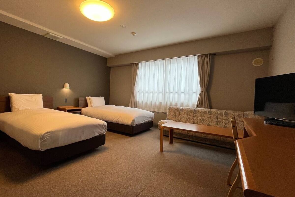 Hotellihuone, jossa on kaksi sänkyä, sohva, televisio ja työpöytä.