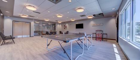 Una sala de conferencias moderna con una mesa de ping pong, asientos cómodos, un gran ventanal y un letrero que dice 'BREWERY'.
