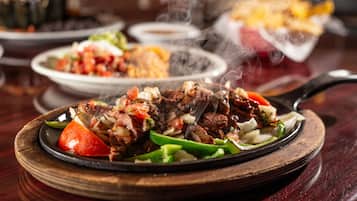 A close-up of a sizzling steak dish with vegetables on a wooden plate.