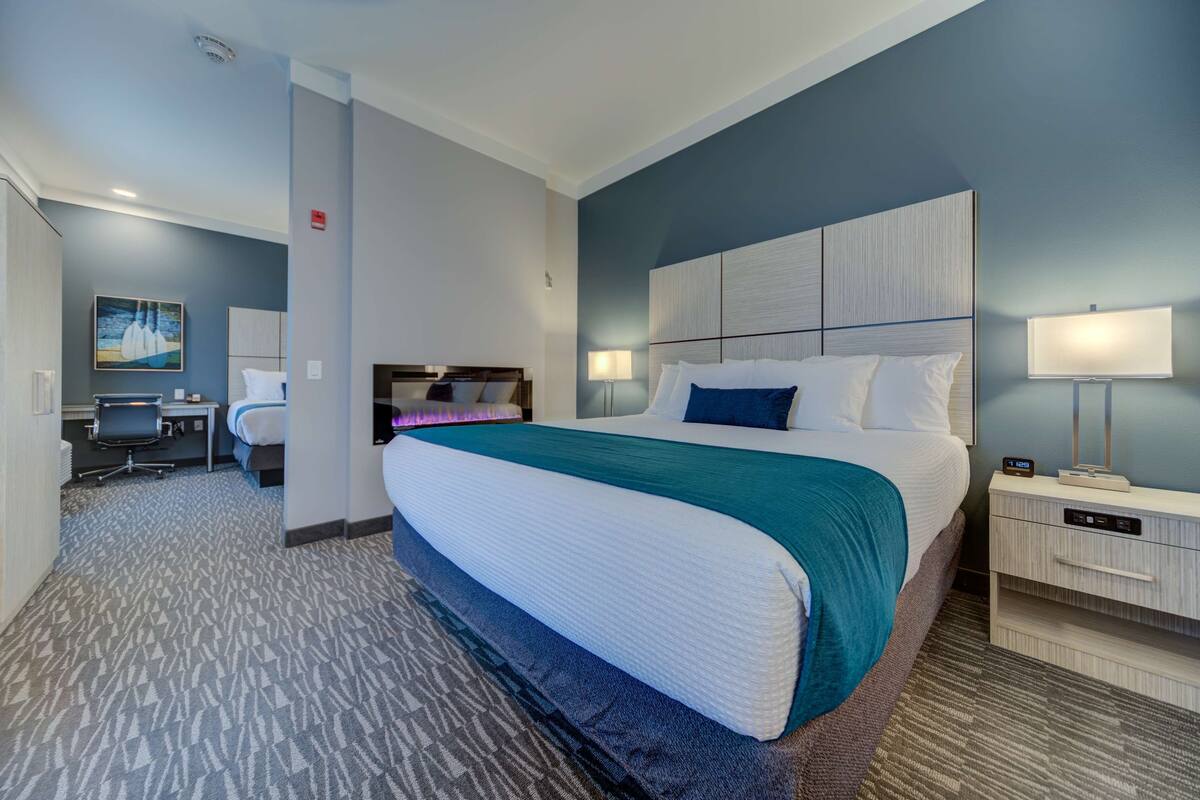 Une chambre d’hôtel avec un grand lit, un bureau, une chaise, une table de chevet et une lampe.