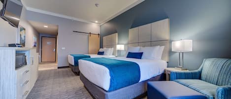A hotel room with two beds, a desk, a chair, and a TV.