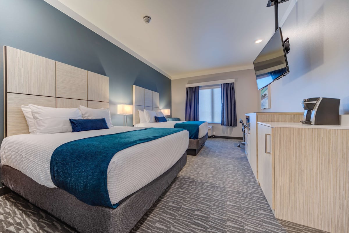Une chambre d’hôtel avec deux lits, un bureau, une télévision et une fenêtre avec des rideaux.