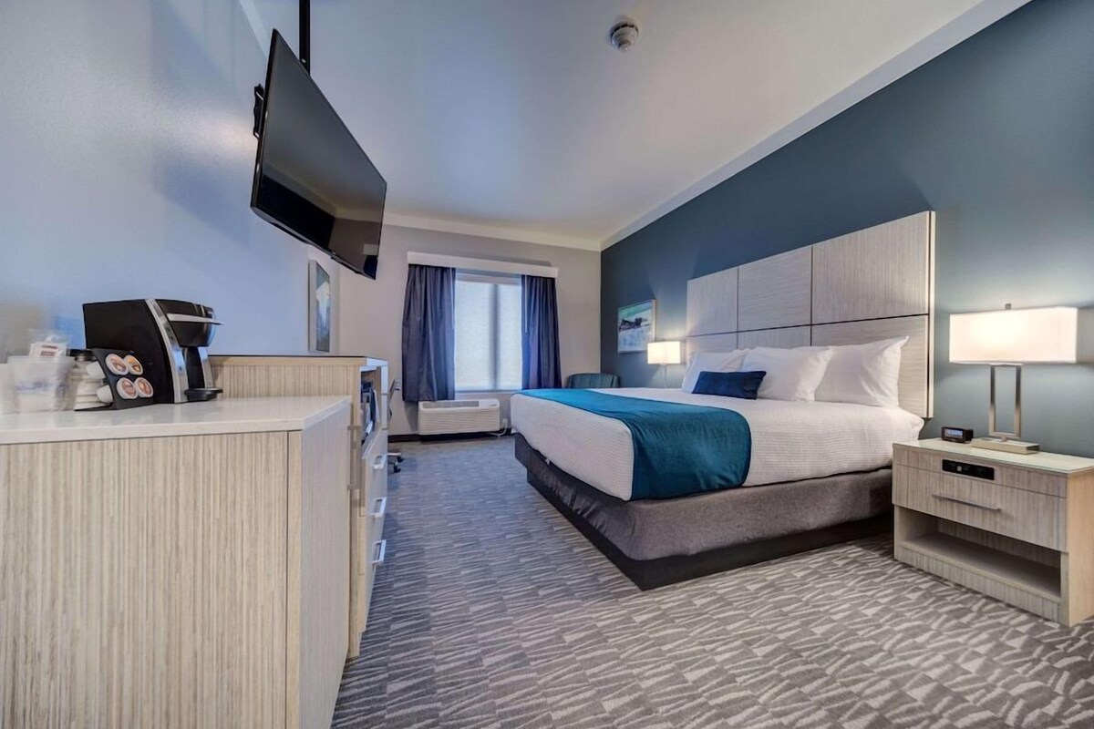A hotel room with a bed, bedside tables, a desk with a computer, a flat-screen TV, and a window with curtains.