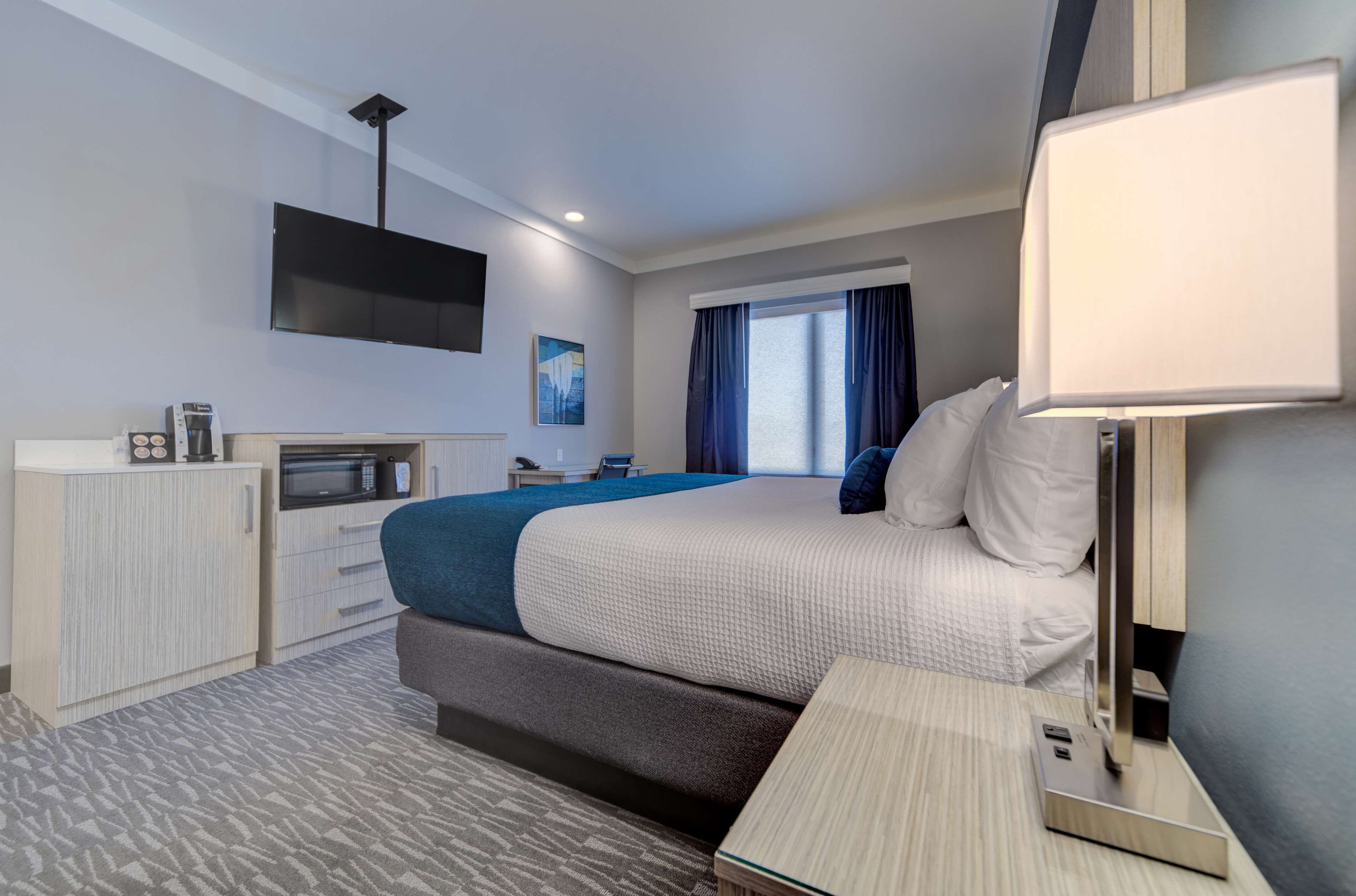 A hotel room with a bed, a desk, a flat-screen TV mounted on the wall, a microwave, and a coffee maker.