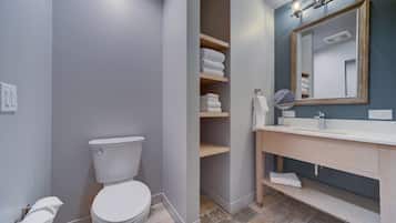 A modern bathroom with a toilet, a vanity with a mirror, and shelves with folded towels.