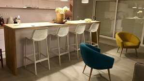 A modern kitchen with white cabinets, a wooden island, and bar stools. There is a yellow chair and a blue chair in the dining area. - Villa Tamara (Jelsa)
