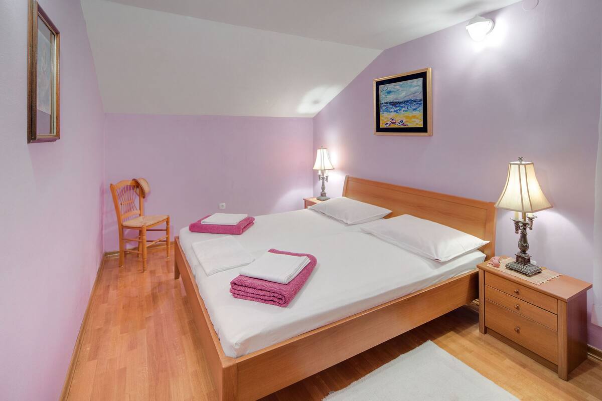 Un dormitorio con una cama de madera, una mesita de noche, una silla, una lámpara y un cuadro en la pared.