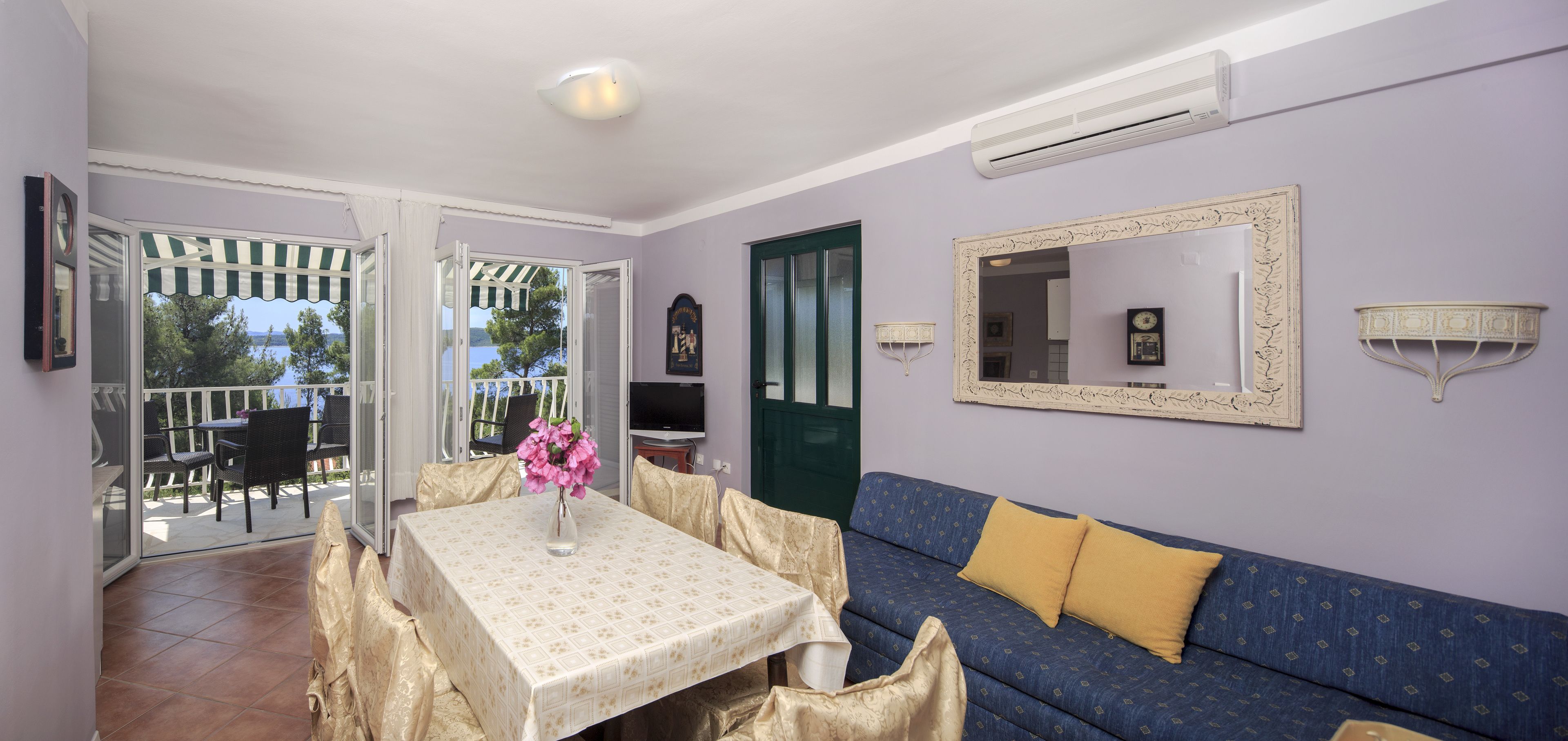 A living room with a sofa, a table with a vase, a TV, and a balcony with chairs.