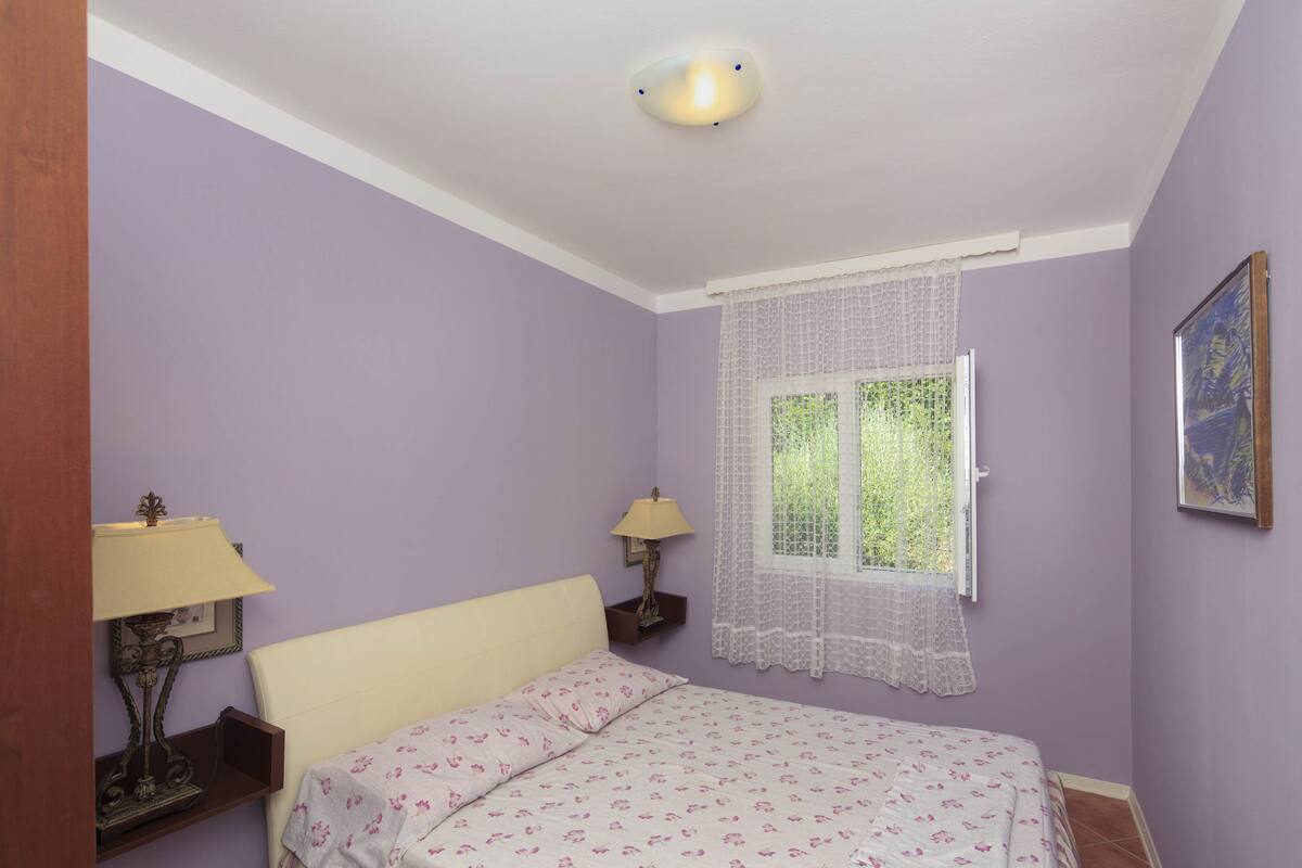 Un dormitorio con cama, dos mesitas de noche, una ventana con cortinas de encaje y una lámpara de pared.