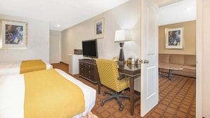 A hotel room with two beds, a desk with a chair, a television, a lamp, and a sofa.
