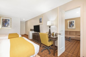 Quarto de hotel com duas camas, uma escrivaninha com cadeira, televisão, luminária e sofá.