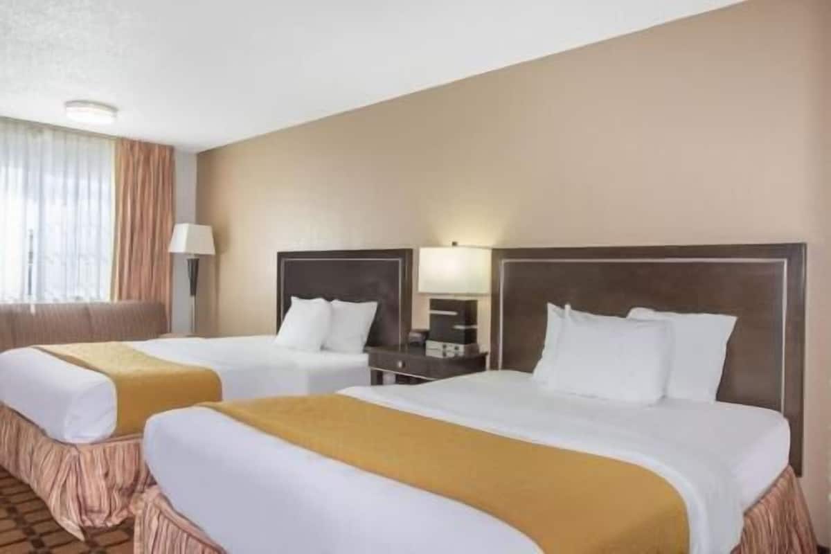 Ein Hotelzimmer mit zwei Betten, einem Nachttisch, einer Lampe und einem Fenster mit Vorhängen.