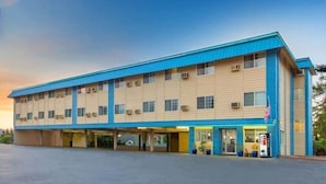 A two-story motel with a blue roof and beige siding, featuring a parking lot and a Pepsi vending machine.