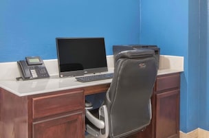 Uma secretária com computador, telefone e impressora num quarto com paredes azuis.