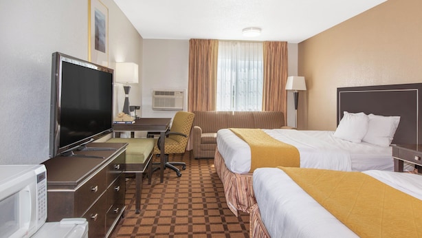 A hotel room with two beds, a desk with a television, a chair, a microwave, and a window with curtains.
