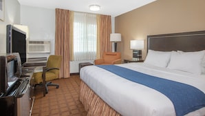 A hotel room with a large bed, a desk with a computer, an air conditioning unit, and a television.
