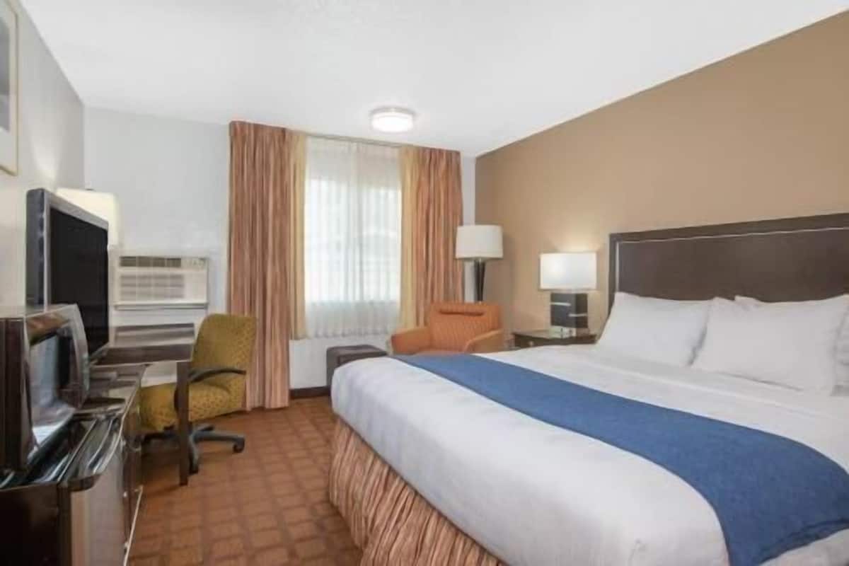 Ein Hotelzimmer mit Bett, Schreibtisch mit Computer, Stuhl, Lampe und Fernseher.