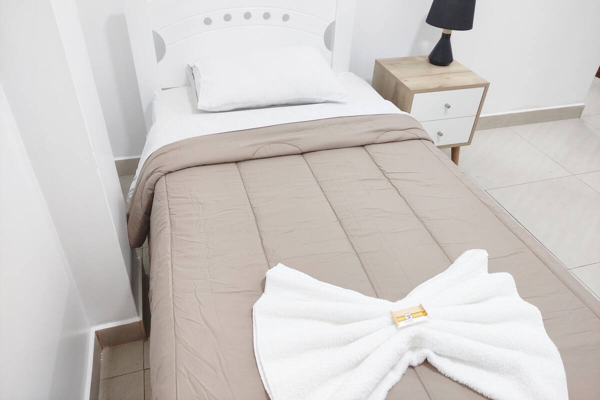 A neatly made bed with a beige comforter and a white towel folded on top.