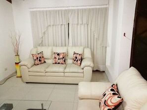 A living room with a beige sofa set, a matching armchair, and a decorative vase with branches. - Maxy's Inn Hotel & Suite (Lima)