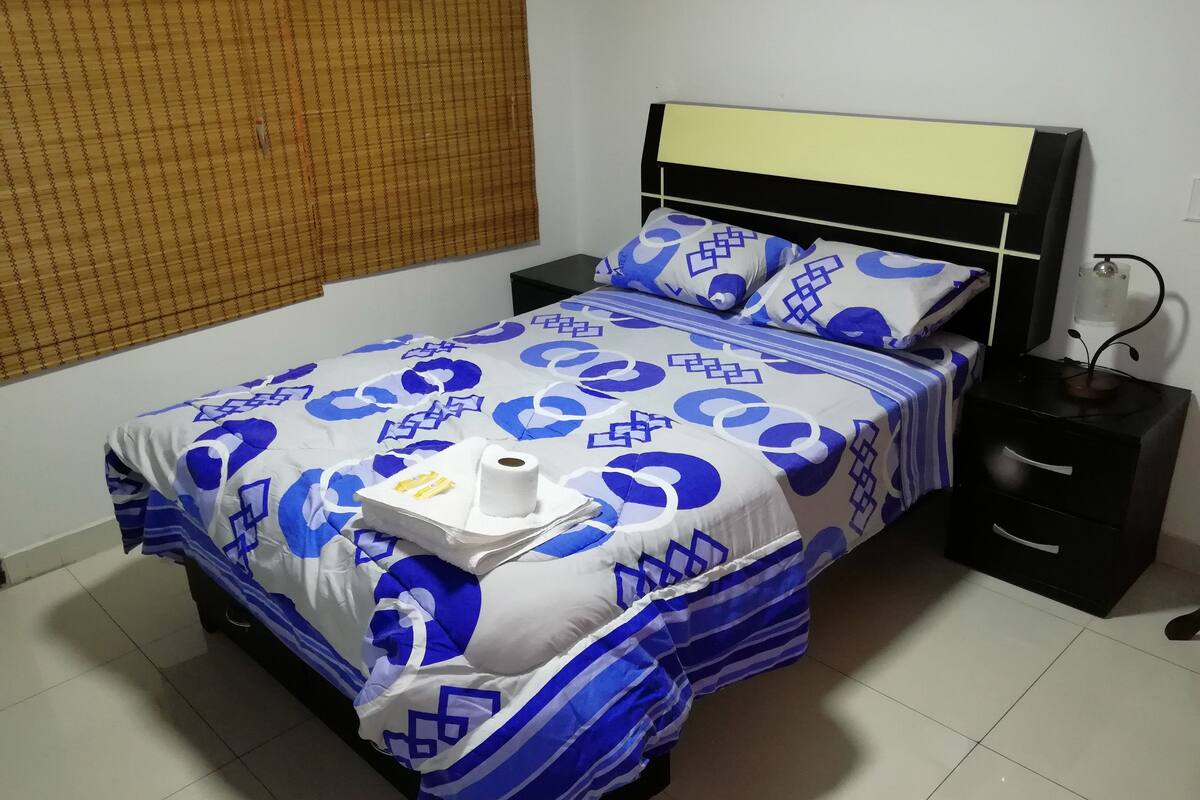 A bed with a patterned bedspread, a bedside table, and a nightstand.