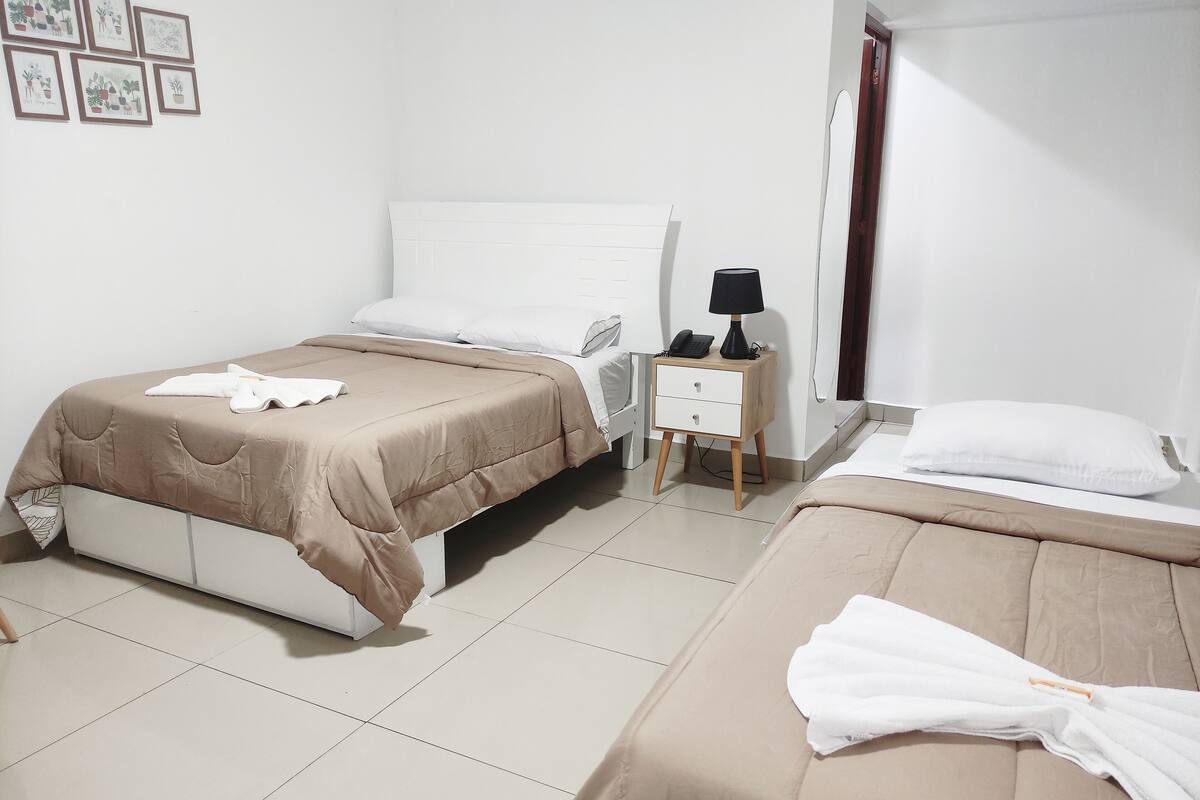 A hotel room with two beds, a bedside table with a lamp, and a small nightstand.