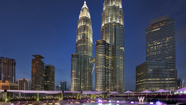 A nighttime view of a cityscape with two prominent skyscrapers, a large illuminated pool area, and surrounding modern buildings. - W Kuala Lumpur (Kuala Lumpur)