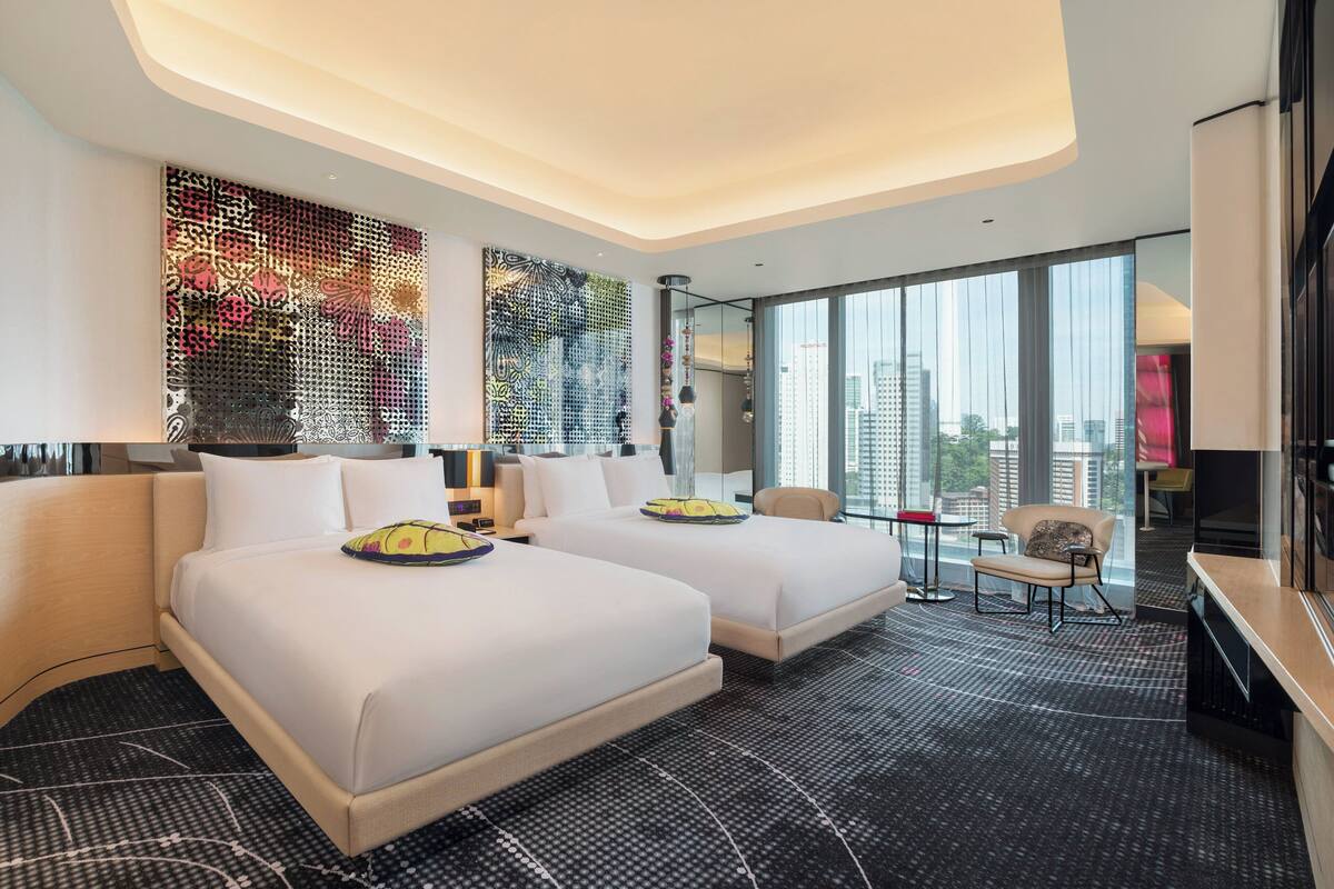 A modern hotel room with two beds, a large window with a city view, and a decorative wall.
