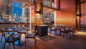 A modern dining area with tables and chairs, a small bar area, and large windows offering a city view. - W Kuala Lumpur (Kuala Lumpur)