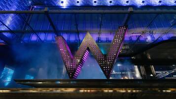 Une grande structure en forme de «
» illuminée, dotée d’une armature métallique et d’une grille de lumières.