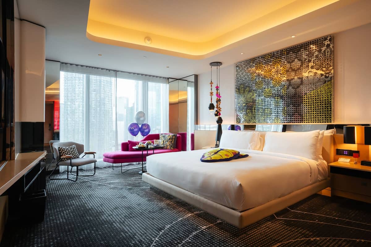 A modern hotel room with a large bed, a desk, a chair, and a sofa.