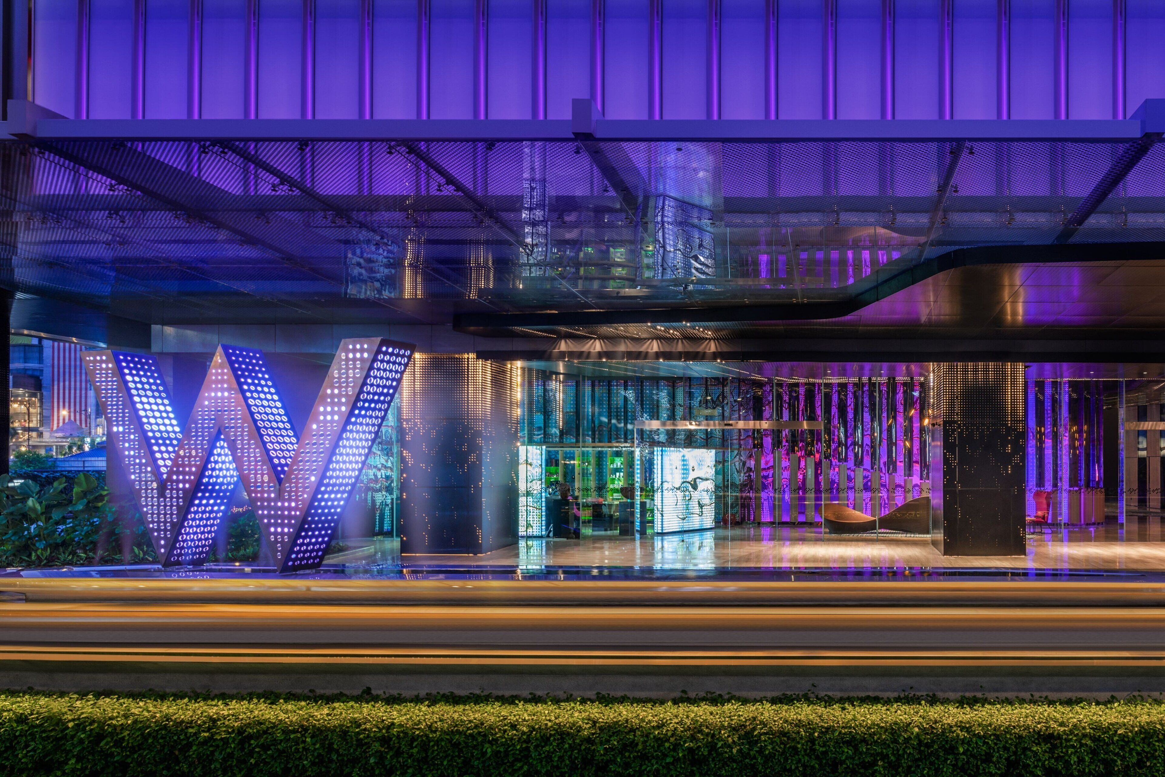 A modern building with a prominent illuminated 'W' sign, a glass facade, and a rooftop terrace.