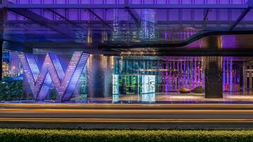 A modern building with a prominent illuminated 'W' sign, a glass facade, and a rooftop terrace.