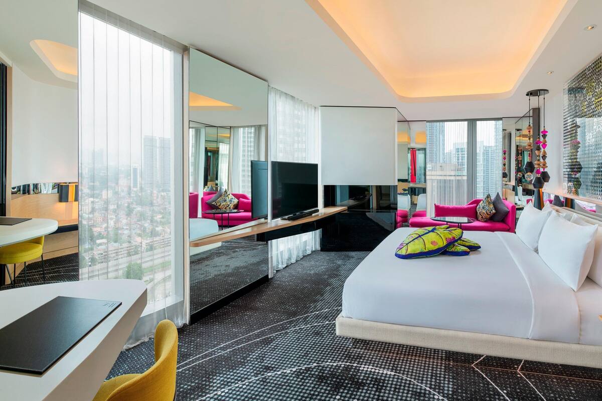 A modern hotel room with a large bed, a desk, a TV, and a city view.