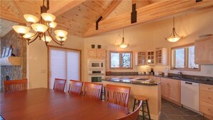 A wooden dining table with chairs, a kitchen with a stone backsplash, and built-in cabinets.