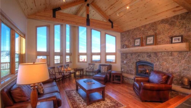 A cozy living room with a fireplace, large windows, and a stone wall.