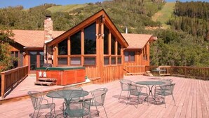 A wooden cabin with a large deck, outdoor seating, and a scenic hillside view.
